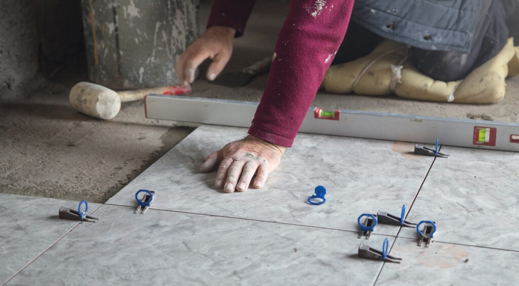 Carreleur posant des carreaux de sol avec un système de nivellement pour un alignement parfait.