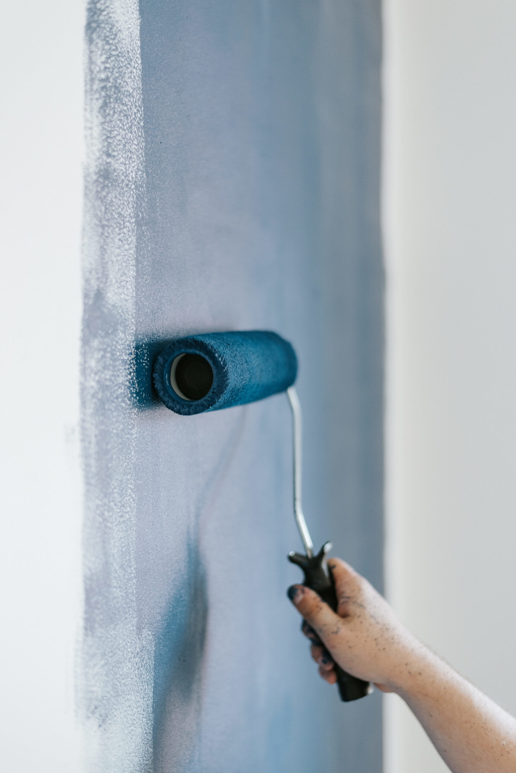 Peintre en bâtiment appliquant de la peinture bleue sur un mur à l'aide d'un rouleau.