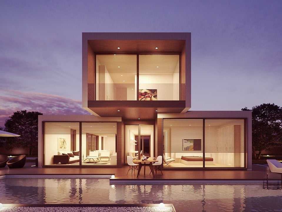 Villa contemporaine au design cubique avec de grandes baies vitrées, une terrasse aménagée et une piscine éclairée au crépuscule.