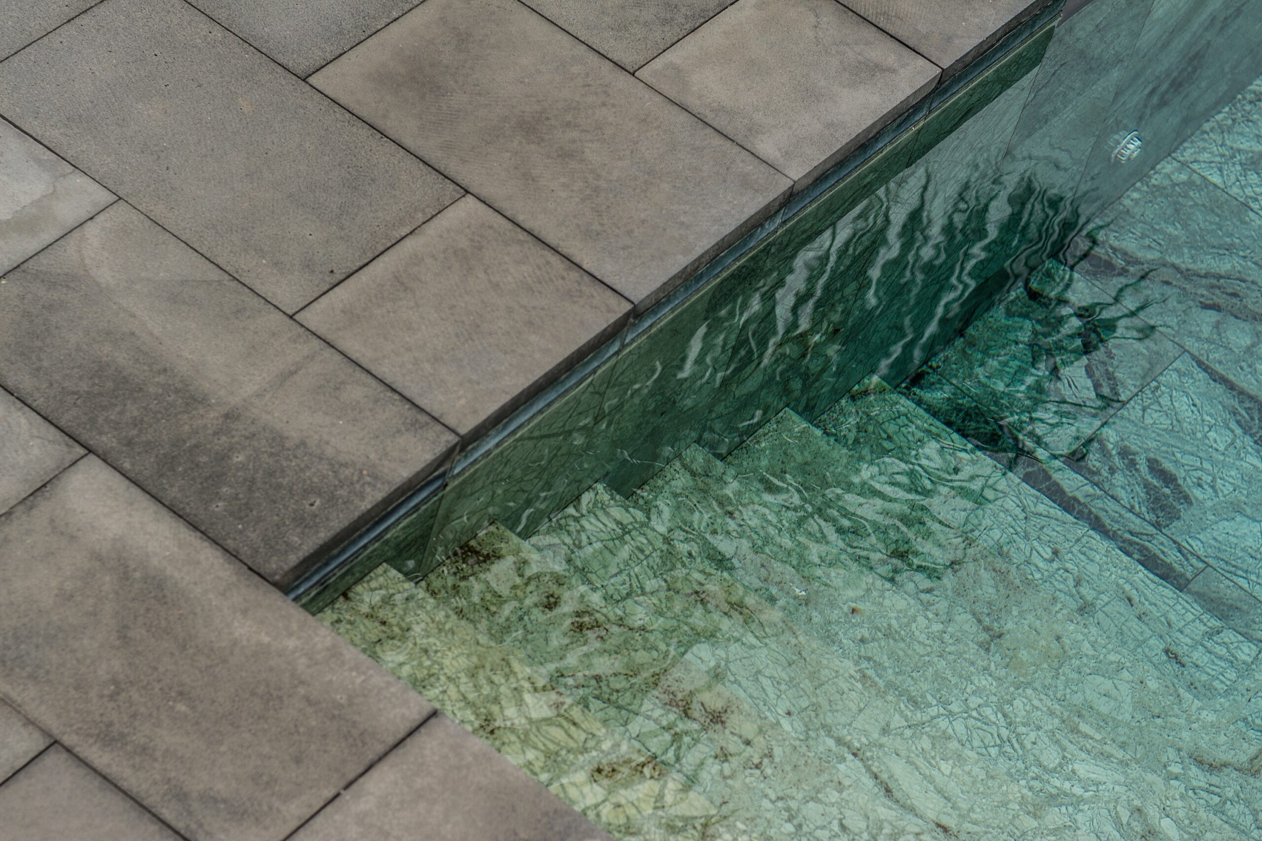 Piscine avec des pavés en béton et un escalier immergé menant vers l'eau claire.