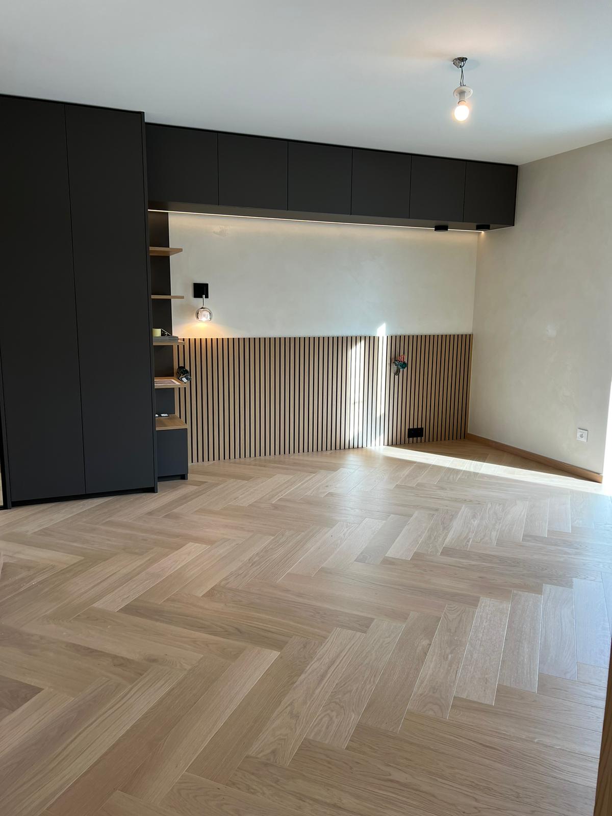 Chambre contemporaine avec un sol en parquet en chevrons, des rangements intégrés noirs et un mur décoré de lattes de bois verticales.