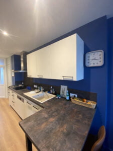 Cuisine moderne rénovée dans un appartement à Thonon avec murs bleus, meubles blancs et plan de travail bois foncé.