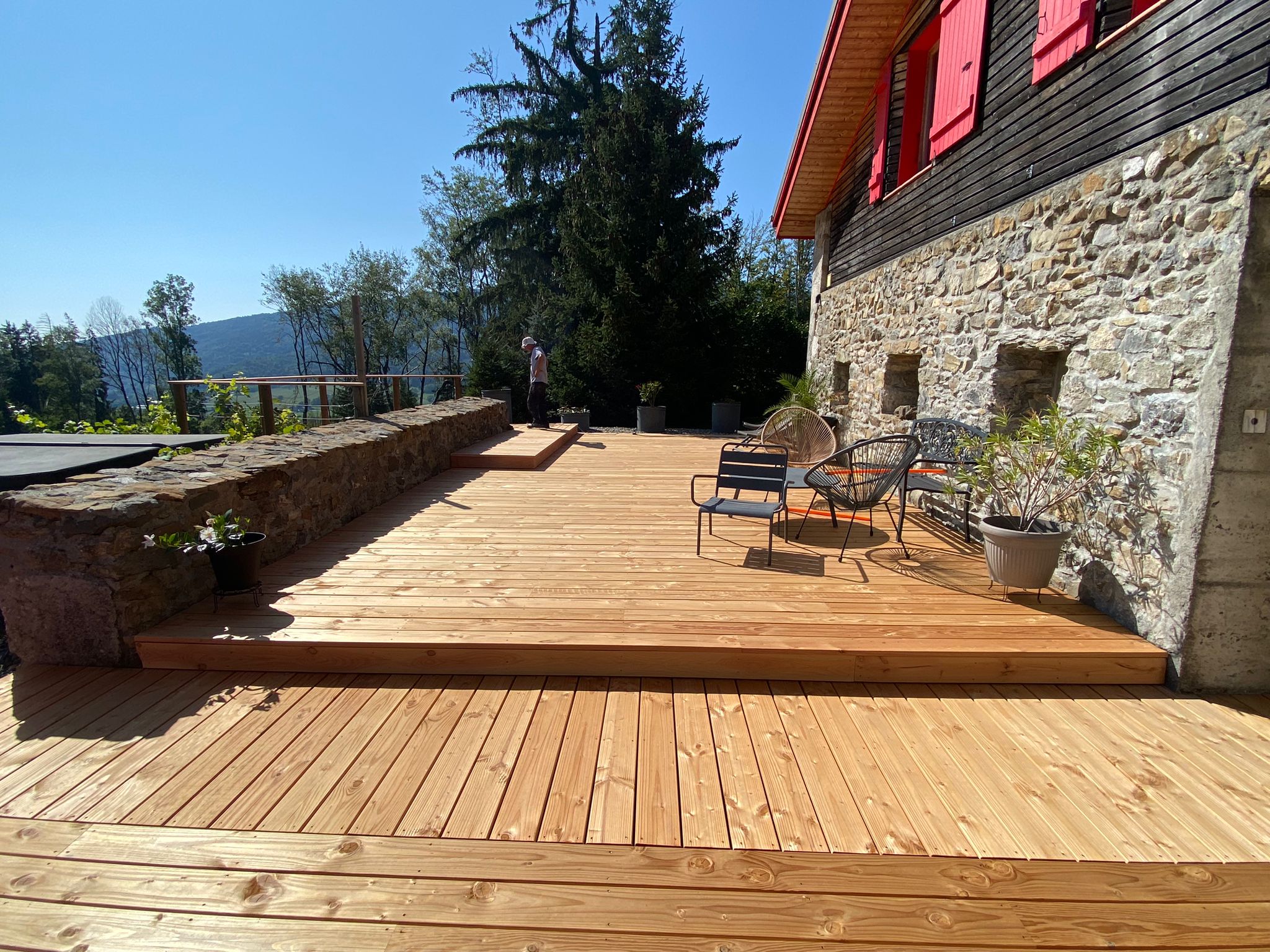 Terrasse extérieure en bois fraîchement rénovée avec vue dégagée sur les montagnes et la forêt environnante.