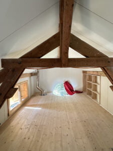 Espace rénové sous les combles avec poutres en bois et puits de lumière.
