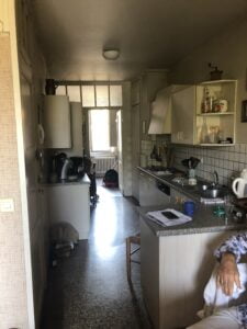 Cuisine ancienne avant rénovation dans un appartement à Thonon, avec mobilier usé et agencement étroit.