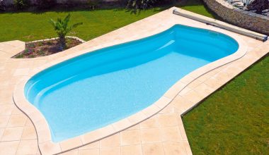 Piscine coque bleue installée dans un jardin avec margelles en pierre et pelouse.