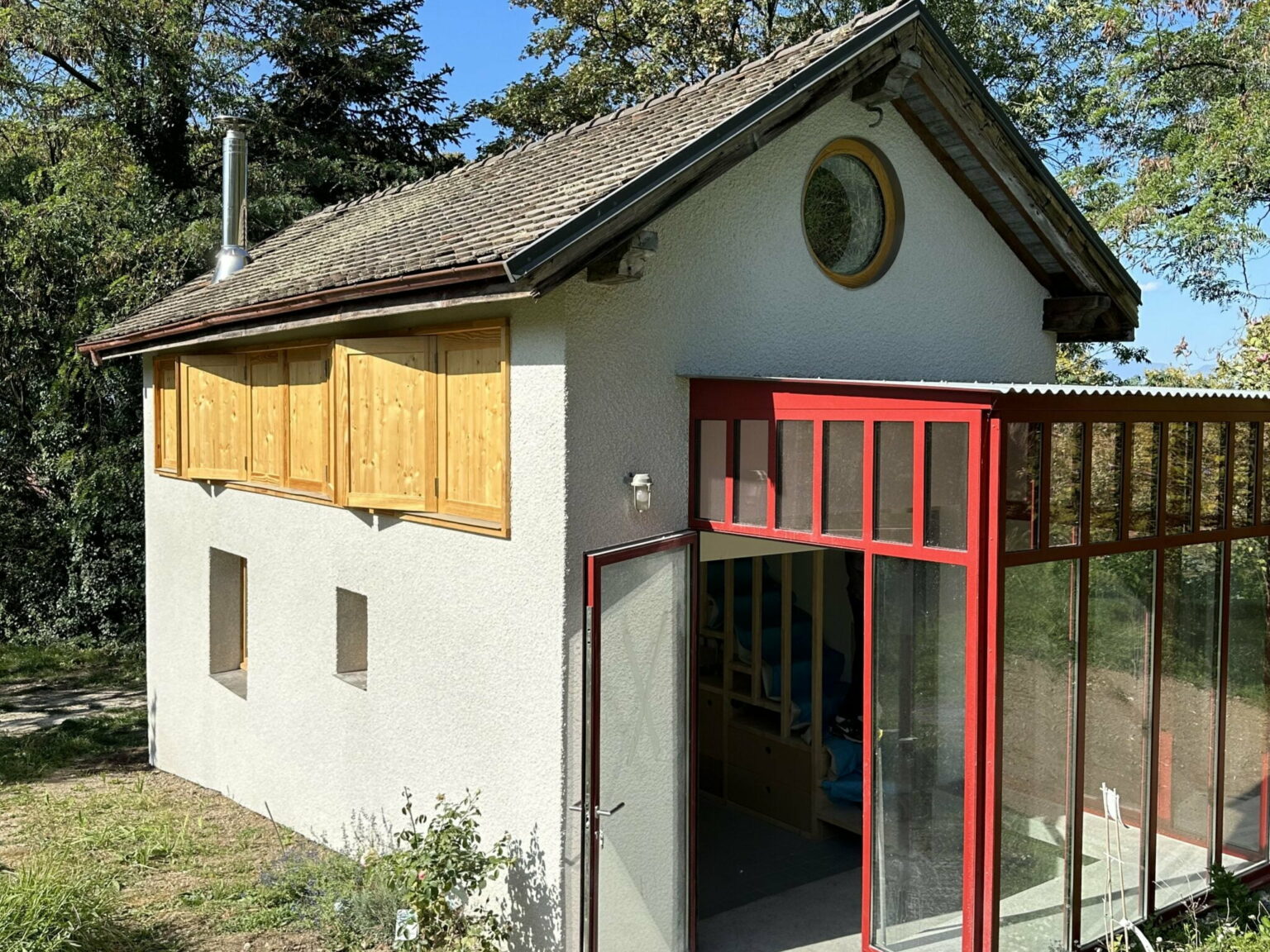 Maison rénovée à Thonon avec façade modernisée, volets en bois et extension vitrée rouge.