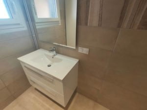 Salle de bain moderne rénovée à Thonon avec meuble vasque blanc et carrelage beige.