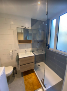 Salle de bains moderne rénovée à Thonon avec douche italienne, meuble vasque et carrelage gris et blanc.
