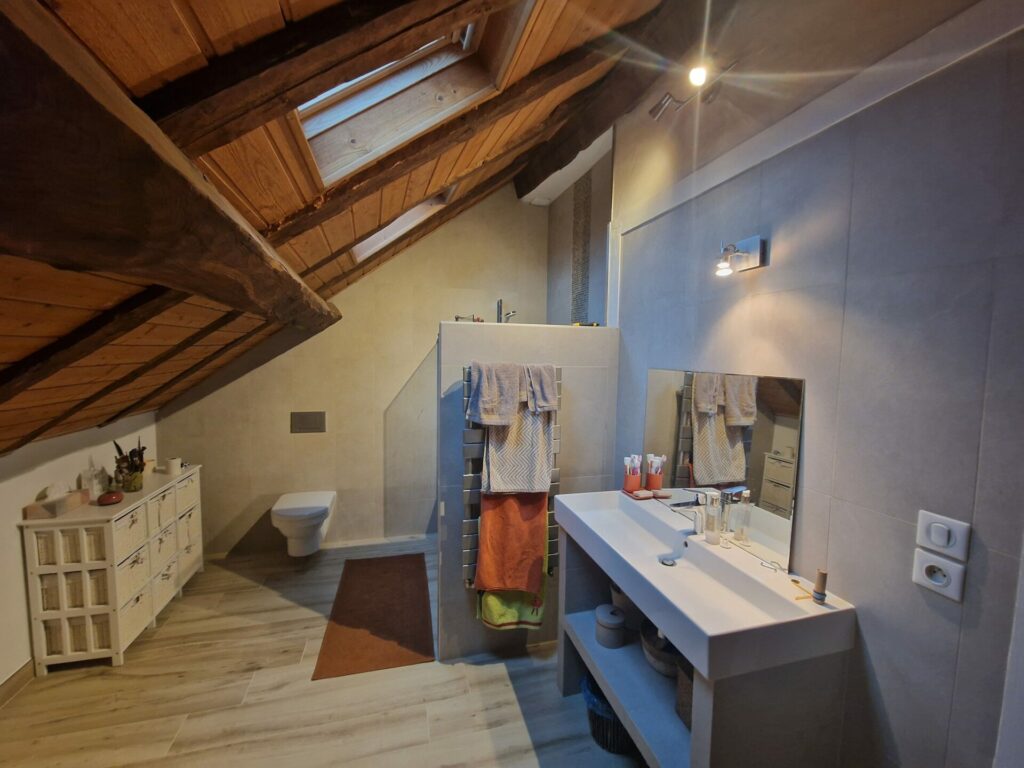 Salle de bains avec vasque, toilettes suspendues et plafond en bois incliné.