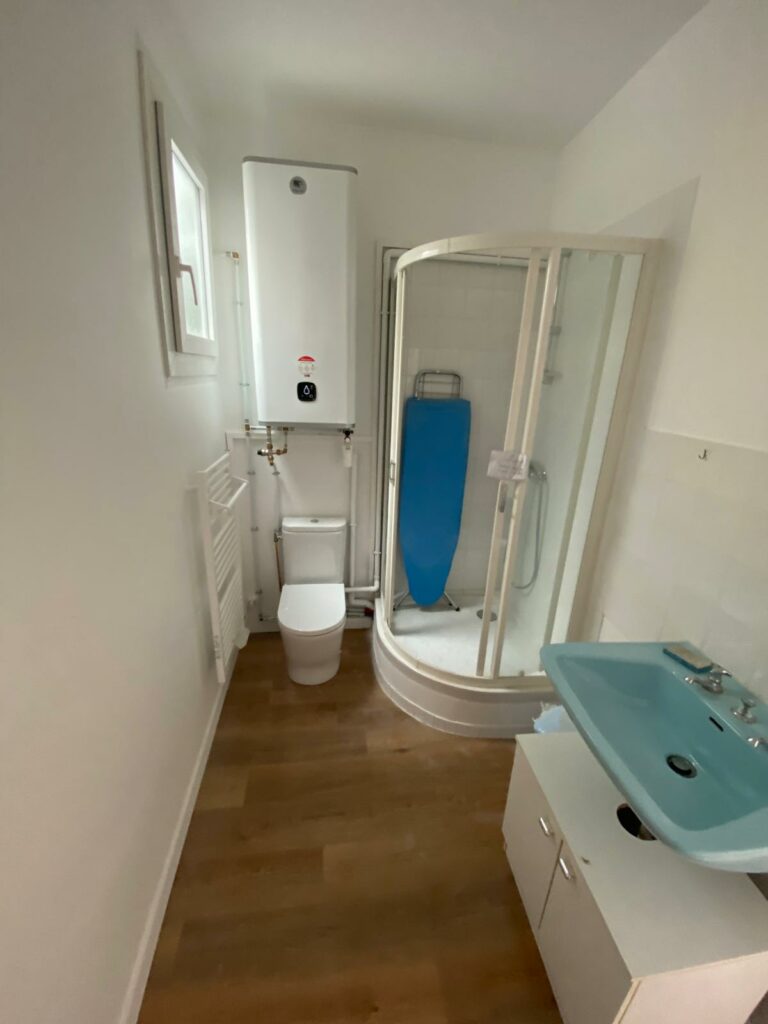 Salle de bain vétuste avec lavabo bleu, murs texturés bleus et sol en lino avant rénovation à Évian