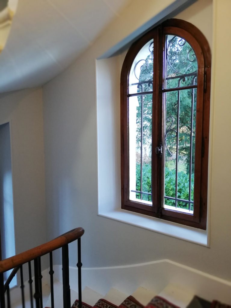 Escalier intérieur rénové à Évian avec fenêtre en bois et vue sur le jardin.