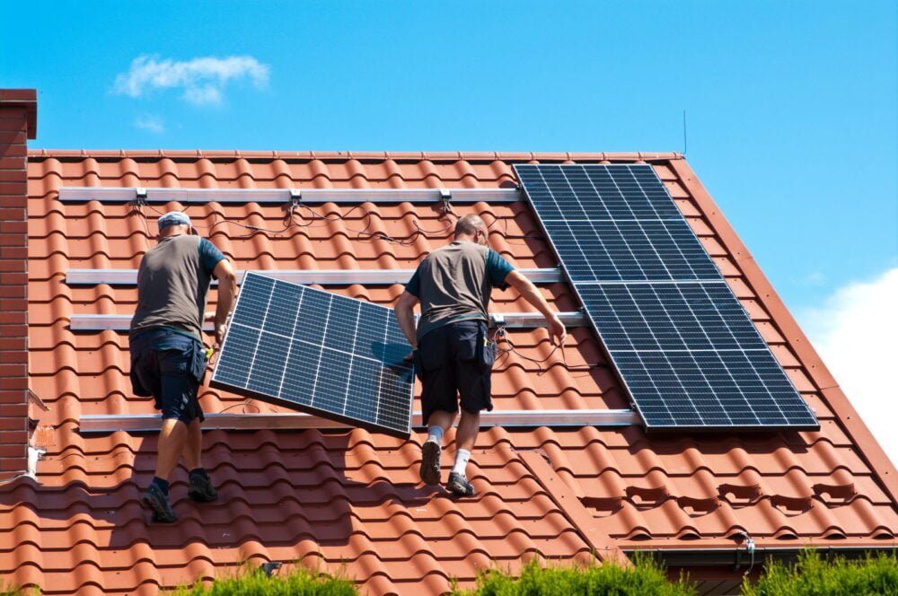 Deux installateurs posent des panneaux solaires sur une toiture en tuiles à Bons-en-Chablais