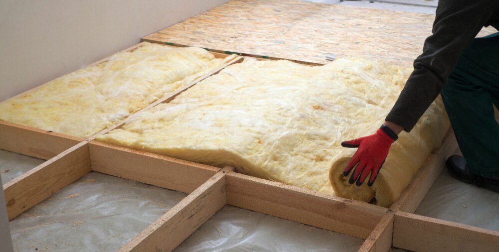 Pose d’isolant en rouleau sous un plancher en bois lors de travaux d’isolation du sol