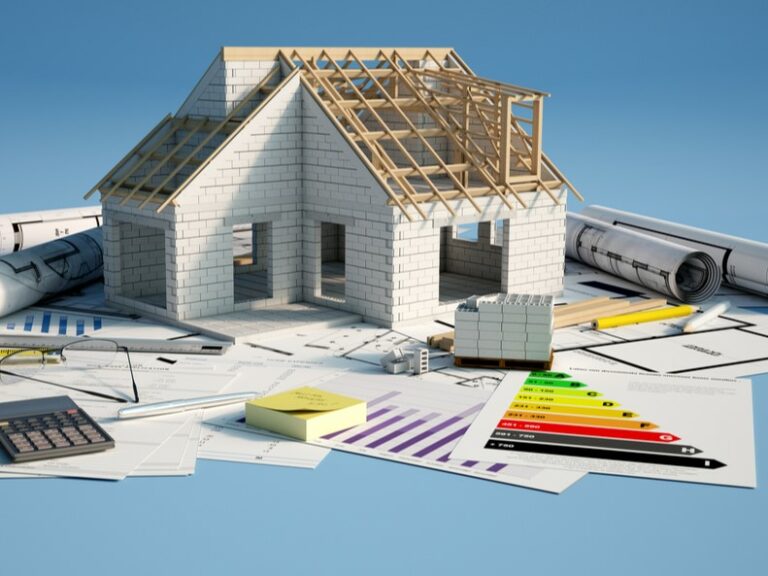 Maquette de maison en construction entourée de documents et plans liés à un projet de rénovation énergétique.