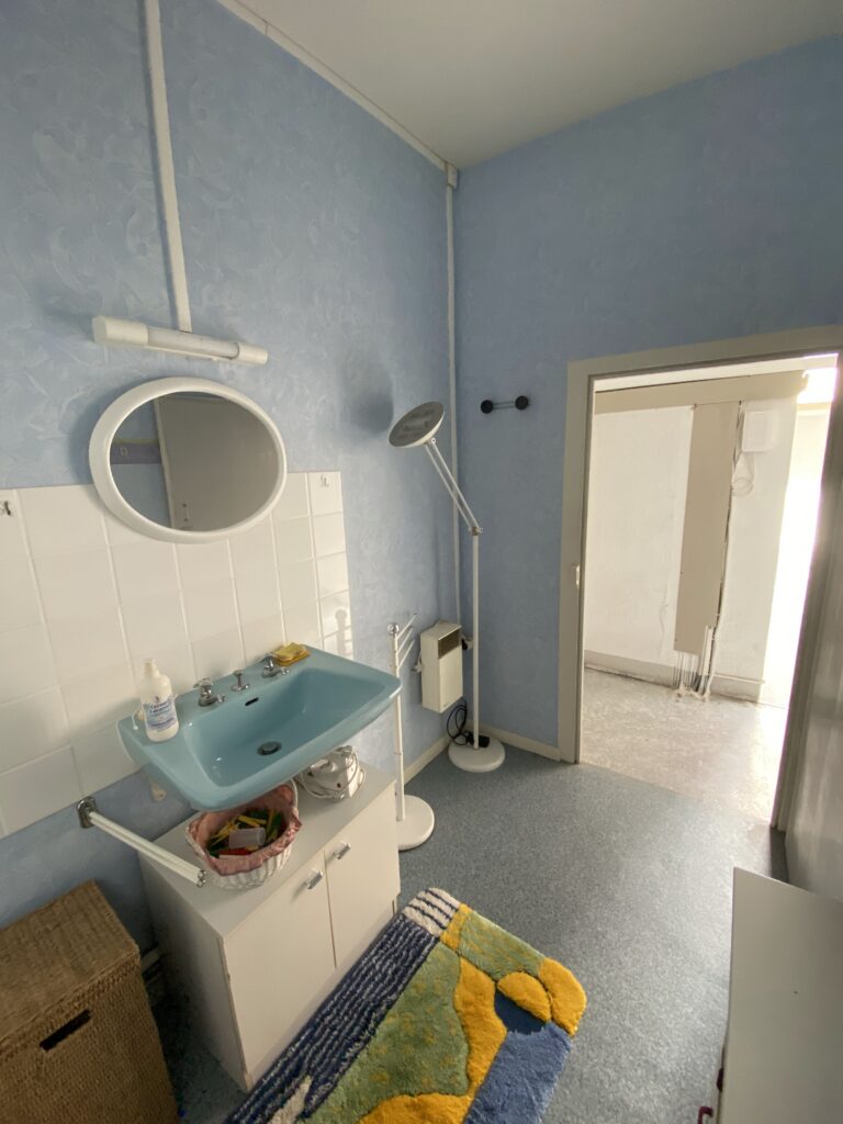Salle de bain complète avec douche arrondie, lavabo bleu et tapis coloré avant rénovation à Évian
