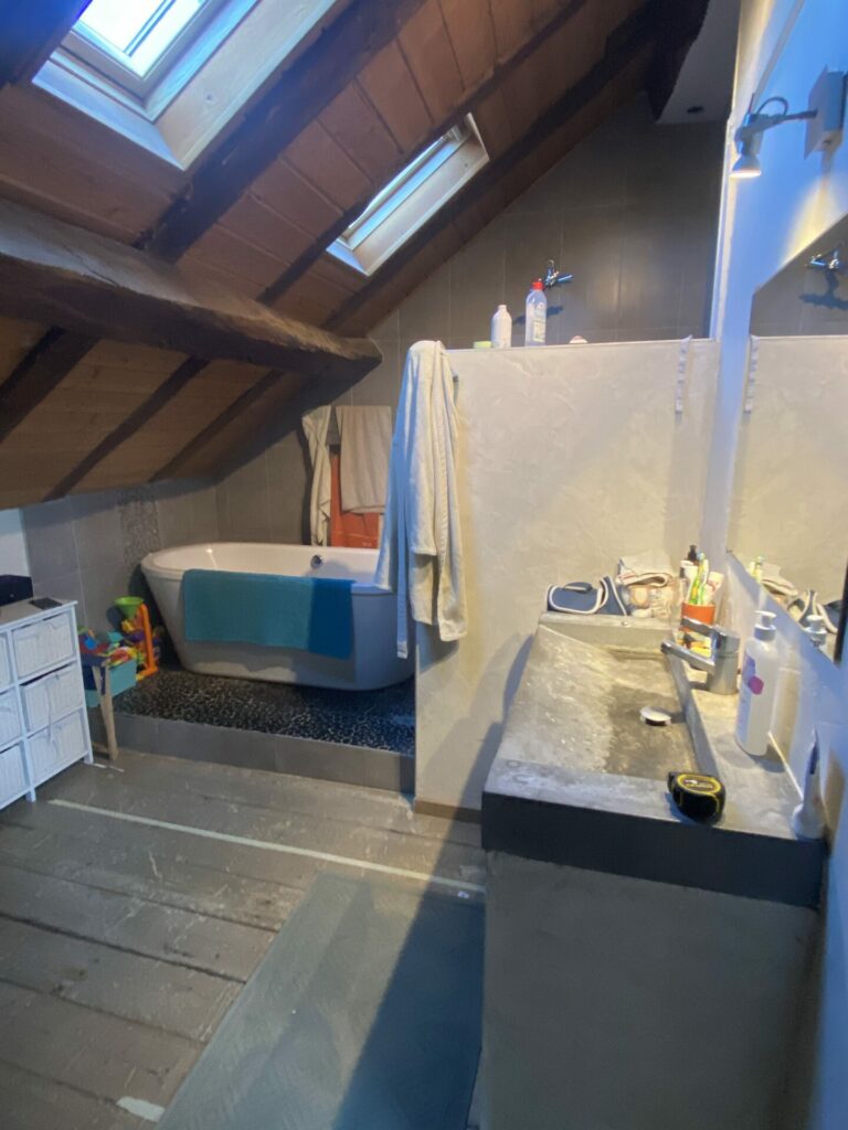 Salle de bains mansardée avec baignoire îlot et vasques sous un plafond en bois.