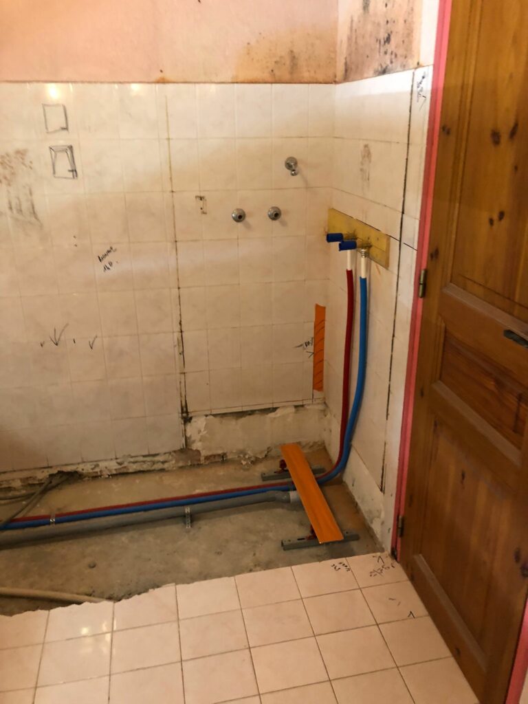 Ancienne salle de bain avec carrelage blanc et canalisations exposées en cours de dépose.