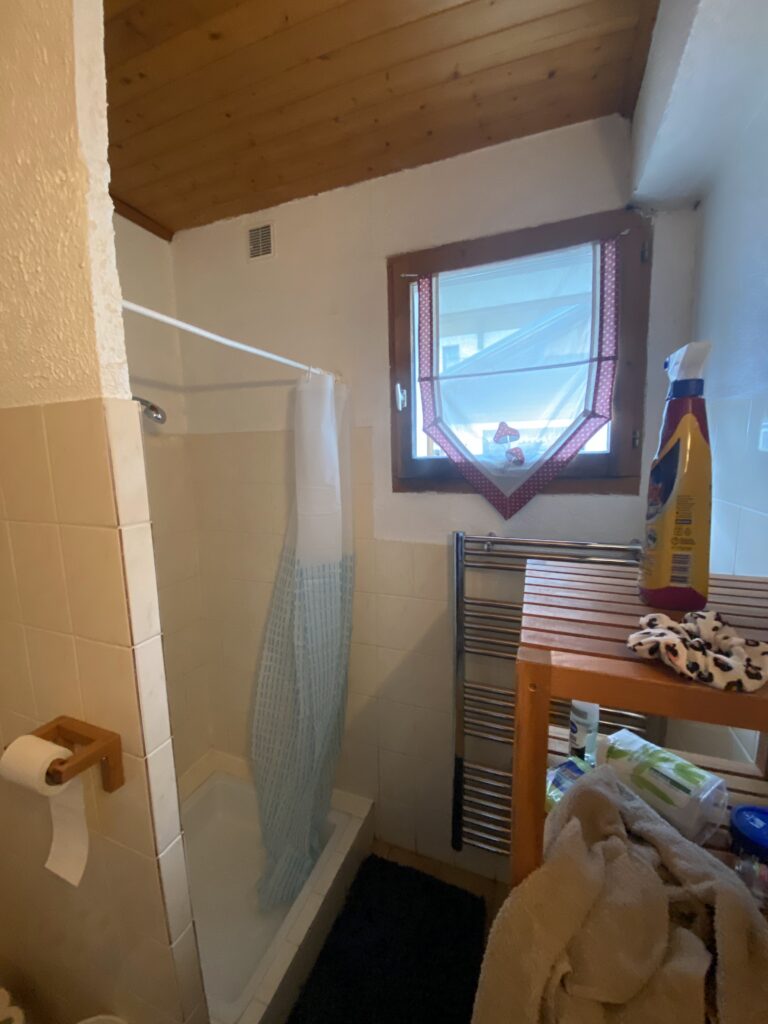 Ancienne salle de bain avec douche fermée par un rideau bleu à Châtel