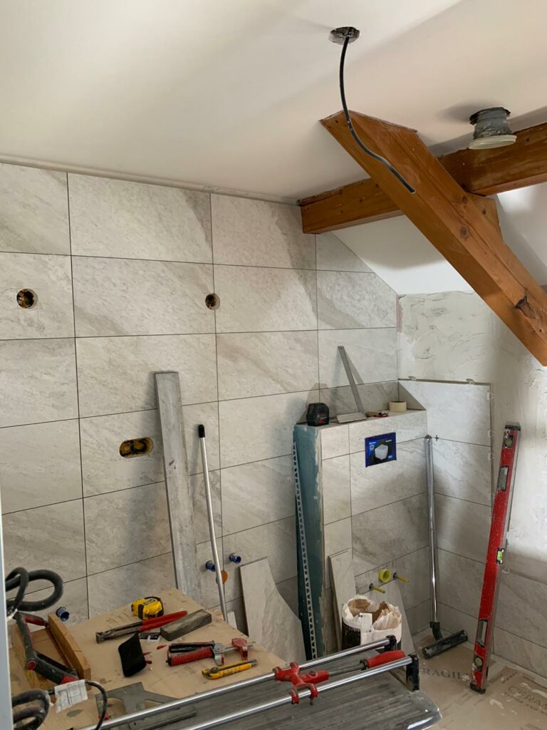 Chantier avec carrelage mural grand format en cours de pose sous rampant de toit.