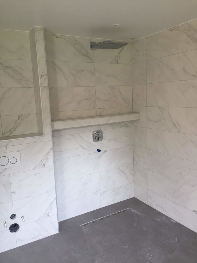 Douche italienne spacieuse avec carrelage mural grand format effet marbre blanc.