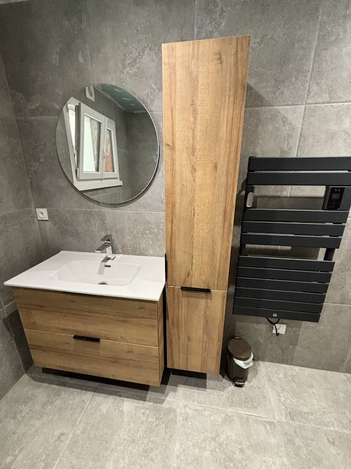 Meuble vasque bois avec miroir rond dans une salle de bain rénovée à Bons-en-Chablais