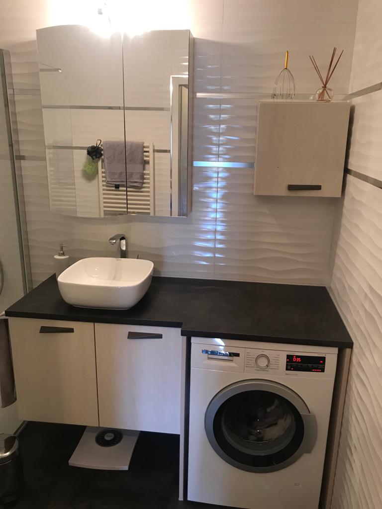 Meuble vasque avec plan de travail et machine à laver intégrée dans une salle de bain moderne.