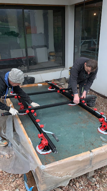 Deux ouvriers installent un grand carreau à l’aide de ventouses sur un chantier.