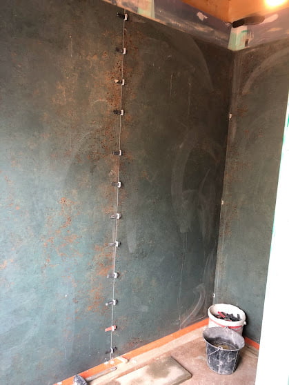 Mur de salle de bain en cours de pose de carrelage grand format.