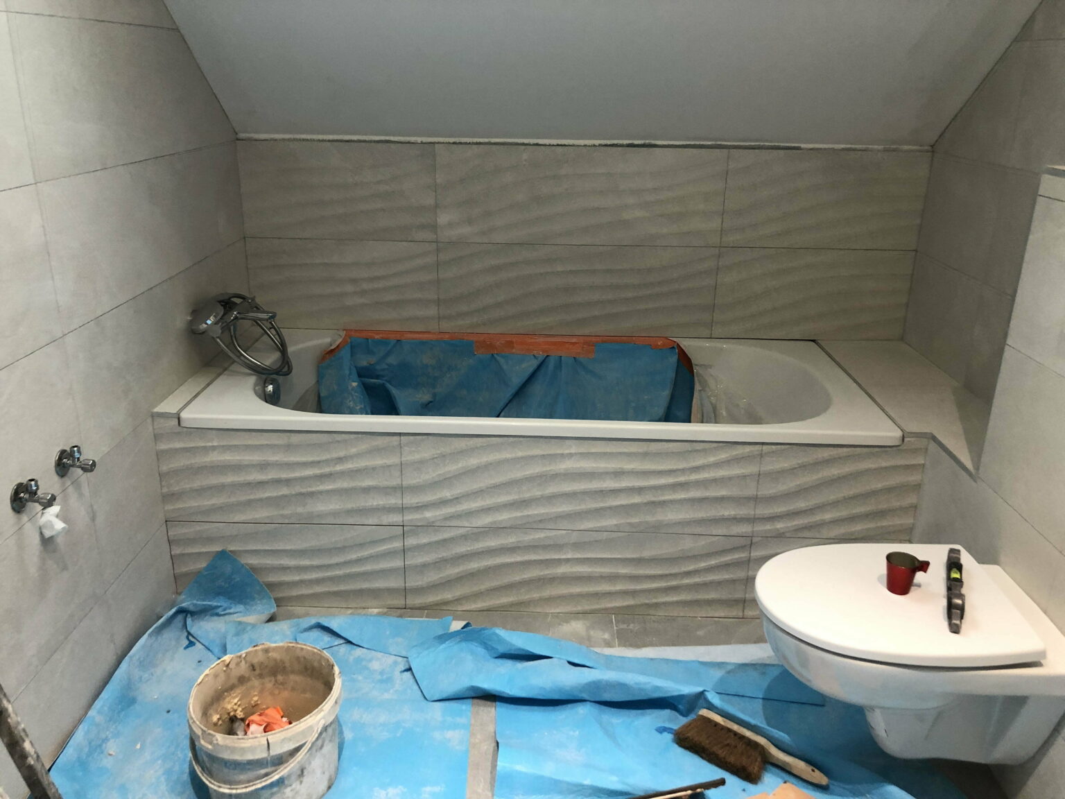 Salle de bain sous combles en rénovation avec baignoire encastrée et WC suspendu.