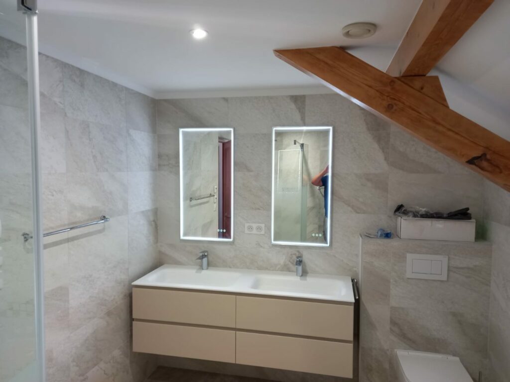 Salle de bain rénovée avec double vasque suspendue et carrelage effet pierre.