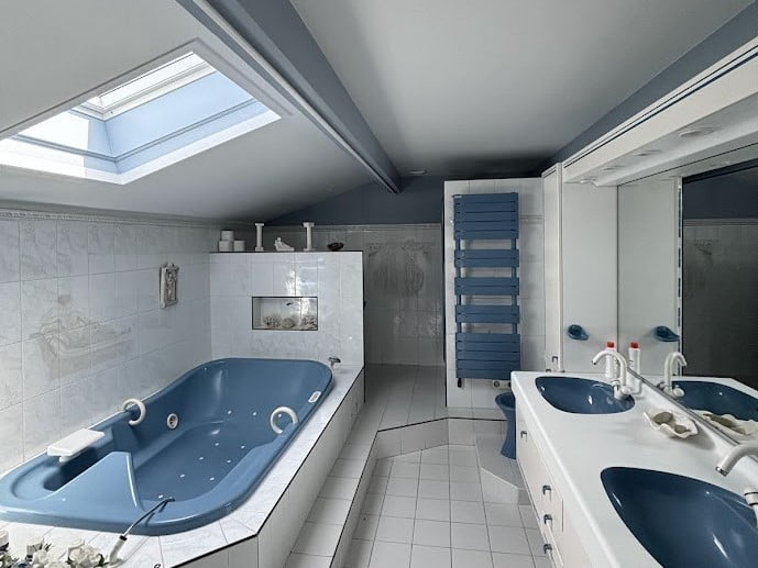 Salle de bains rénovée avec meubles bleus, grande baignoire et lumière naturelle.