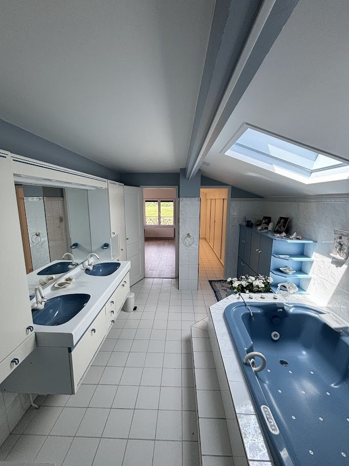 Salle de bains rénovée avec baignoire bleue, double vasque et verrière de toit.