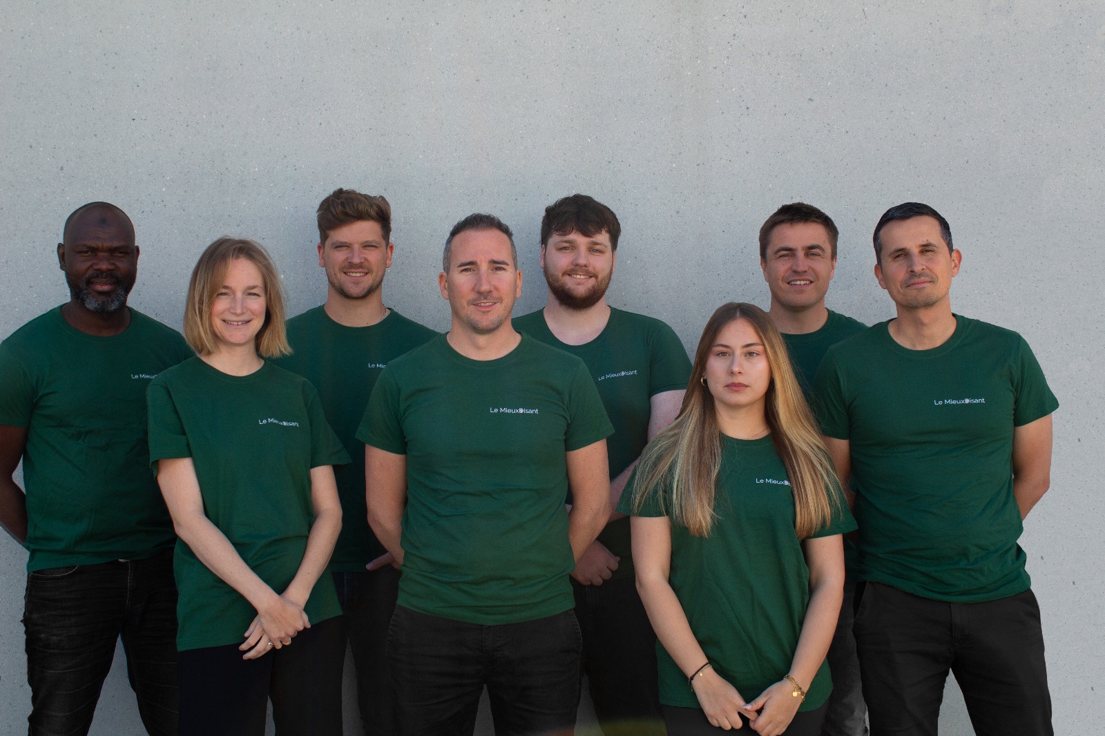 Huit membres de l’équipe LeMieuxDisant posent ensemble devant un mur gris, tous portant un t-shirt vert avec le logo de l’entreprise.