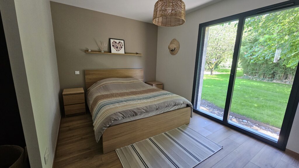 Chambre parentale avec lit en bois, déco naturelle et baie vitrée donnant sur un jardin à Douvaine.