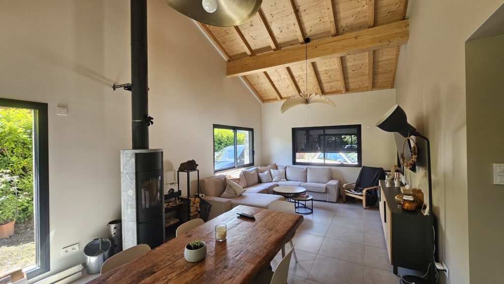 Salon avec plafond cathédrale, poêle à bois et grande baie vitrée dans une maison moderne à Douvaine.