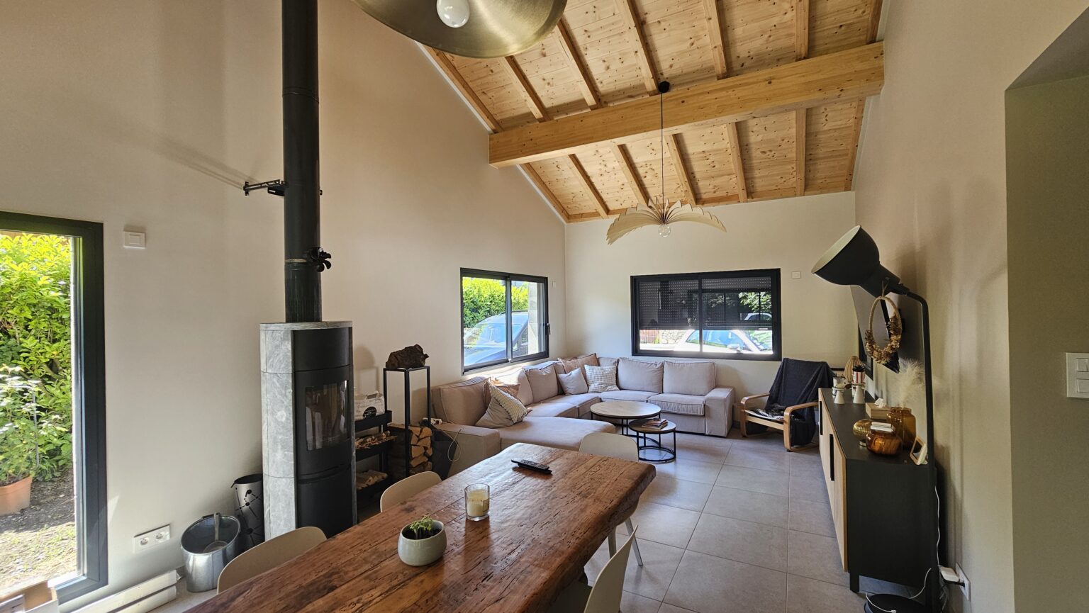 Salon avec plafond cathédrale, poêle à bois et grande baie vitrée dans une maison moderne à Douvaine.