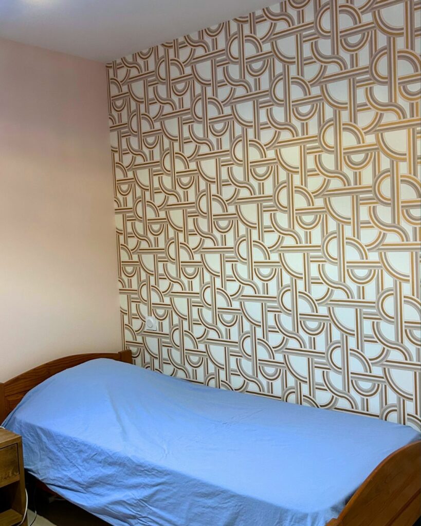 Chambre rénovée dans une maison ancienne à Bons-en-Chablais, avec mur peint en rose doux et papier peint graphique rétro.
