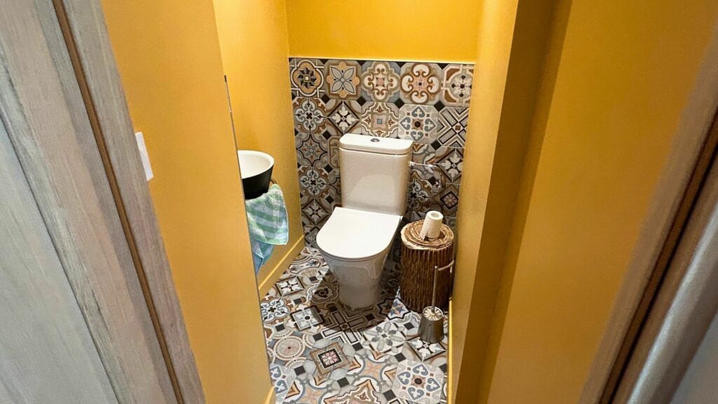 Toilettes rénovées dans une maison ancienne à Bons-en-Chablais, avec murs jaunes et carrelage graphique esprit azulejos.