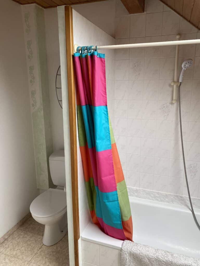 Salle de bain d’origine sous les combles avec baignoire et rideau coloré