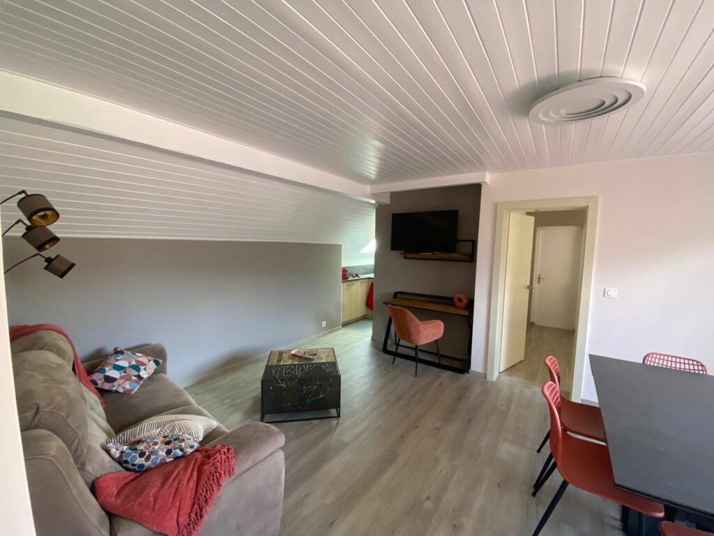 Coin bureau avec chaise en velours rose, bureau en bois et télévision murale dans un appartement rénové à Bons-en-Chablais