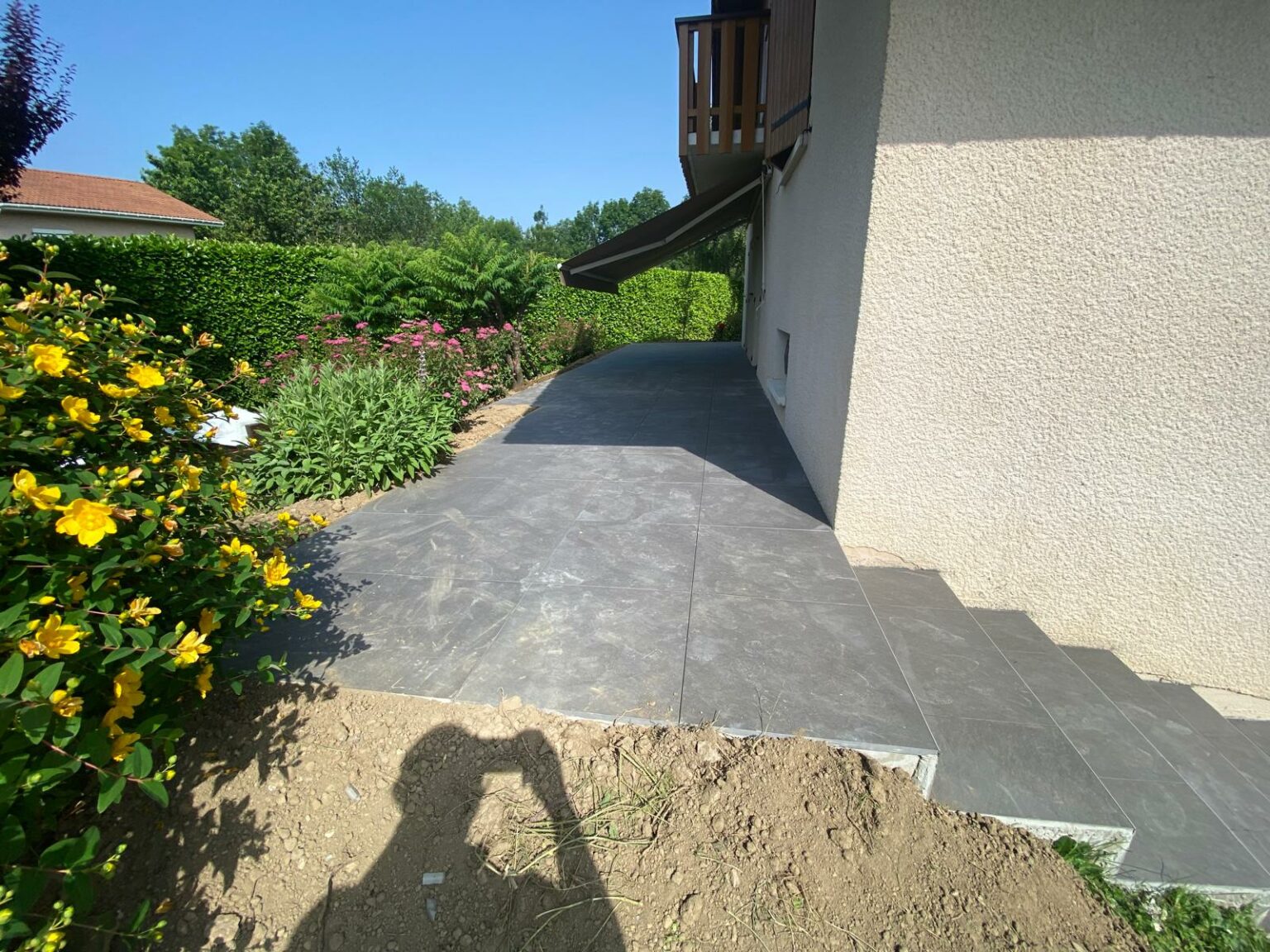 Terrasse en carrelage moderne entourée de massifs à Reignier