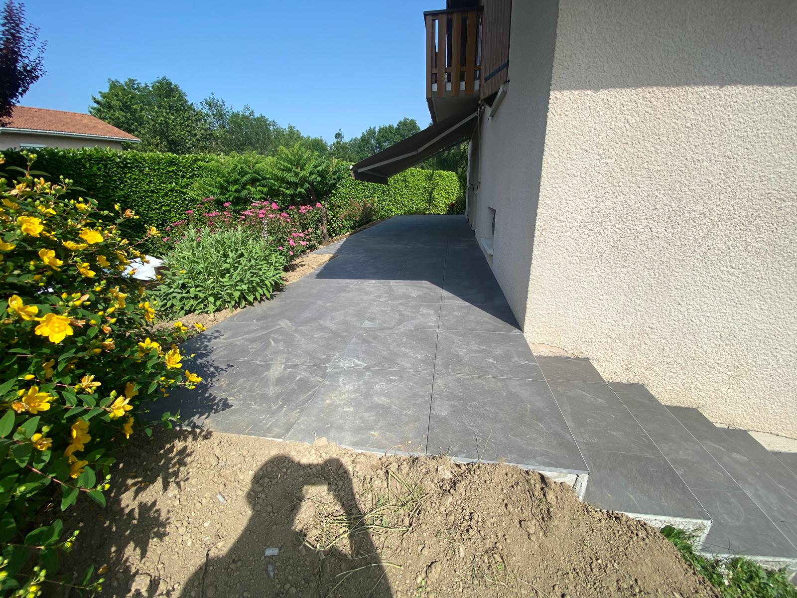 Terrasse en carrelage moderne entourée de massifs à Reignier