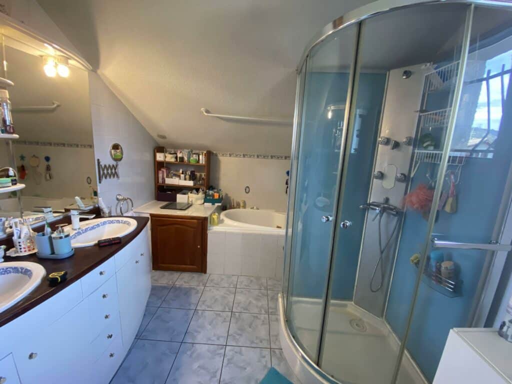 Salle de bains ancienne à Douvaine avant rénovation avec double vasque, douche cabine et baignoire d’angle.