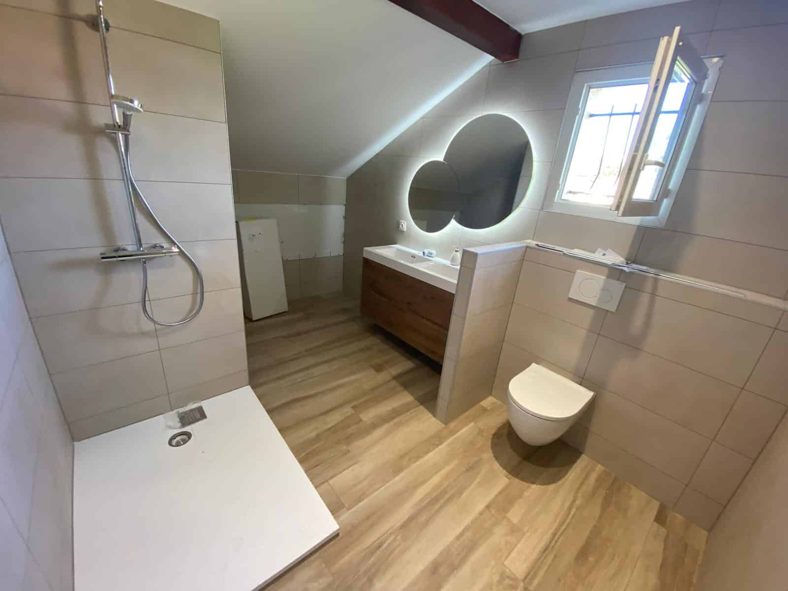 Salle de bains rénovée à Douvaine avec douche à l’italienne, double vasque moderne et carrelage effet bois.