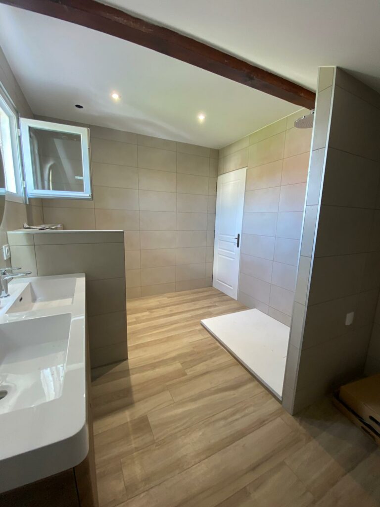 Salle de bains moderne rénovée à Douvaine avec WC suspendu, vasque design et miroir lumineux rond.