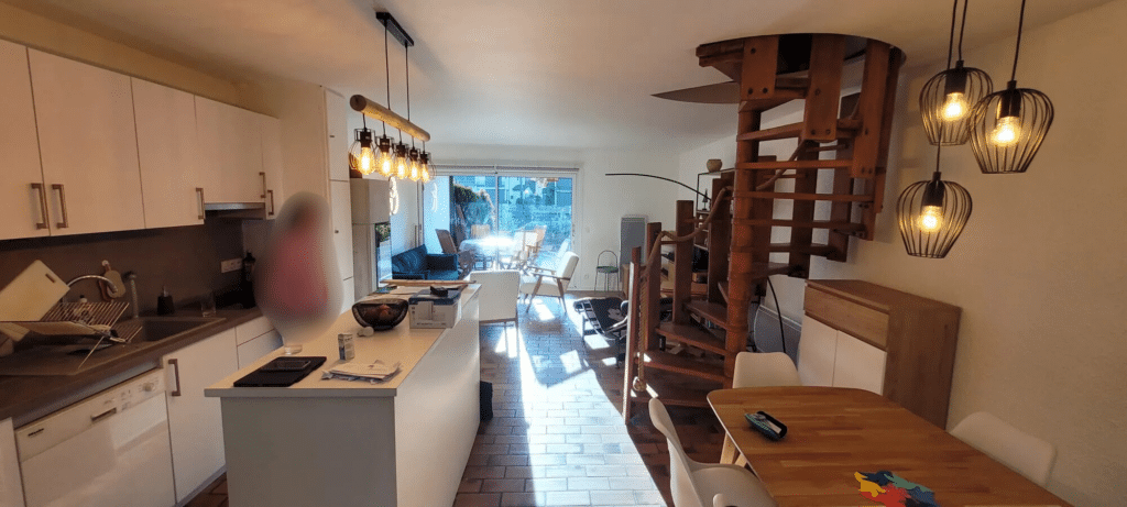Vue sur une cuisine ouverte blanche et moderne donnant sur un séjour lumineux lors d'une rénovation d'intérieur à Thonon-les-Bains.